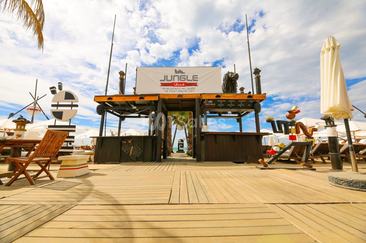Entrée d'un restaurant de plage en bois avec une enseigne ’Jungle’, entourée de décorations nautiques et parasols.