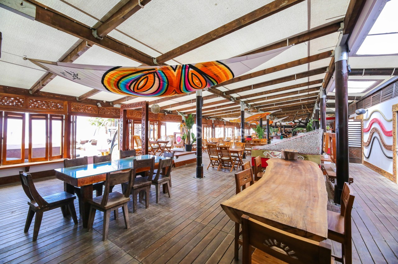 Salle de restaurant en bois avec tables, chaises et décorations colorées sous un toit ouvert.