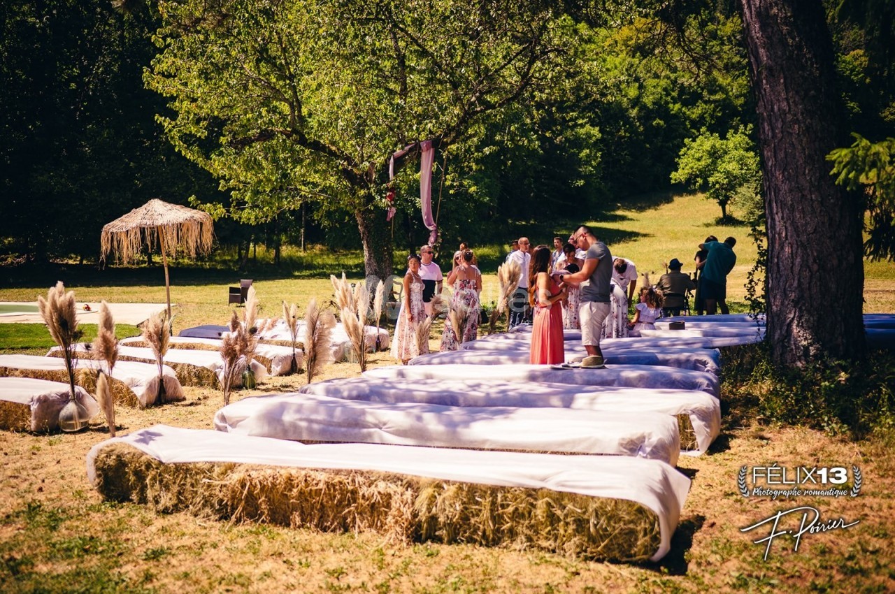 Des bancs en bottes de paille recouverts de tissu blanc disposés en extérieur pour une cérémonie champêtre.