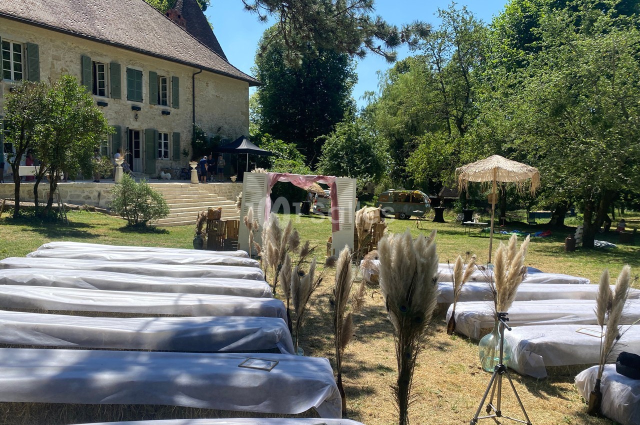 Chaises alignées en extérieur devant une maison ancienne, décorées pour un événement avec des herbes de la pampa.