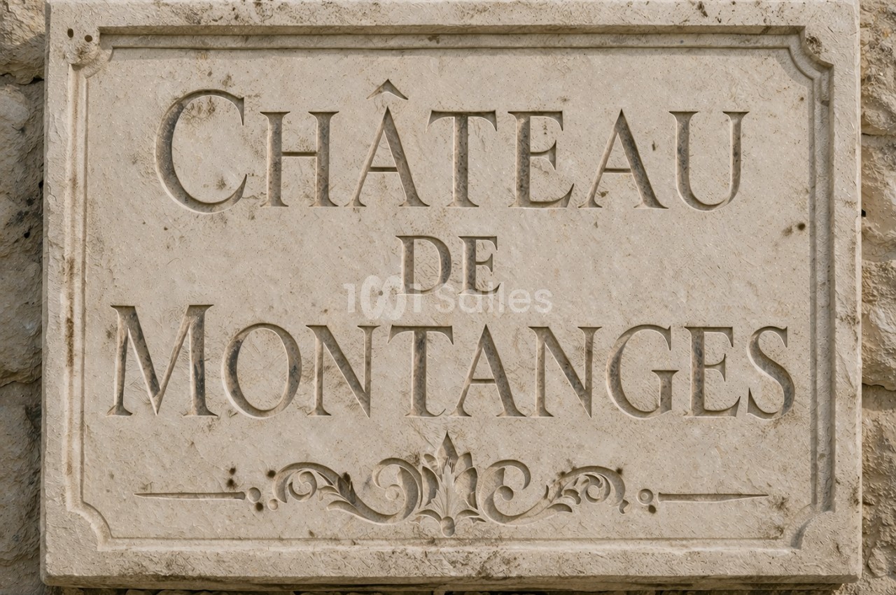 Plaque en pierre gravée indiquant ’Château de Montanges’, fixée sur un mur en pierre.