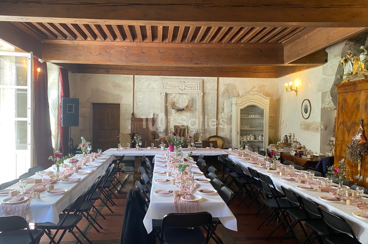 Salle de réception avec tables dressées pour un événement, décor rustique avec poutres apparentes et mobilier ancien.