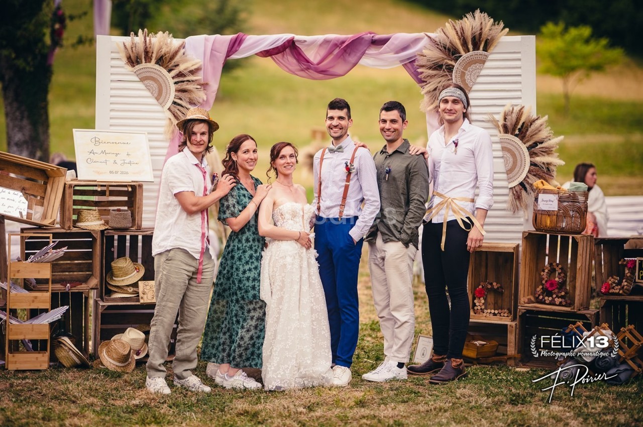 Un groupe de personnes posant devant une arche décorée de fleurs séchées dans un cadre champêtre.