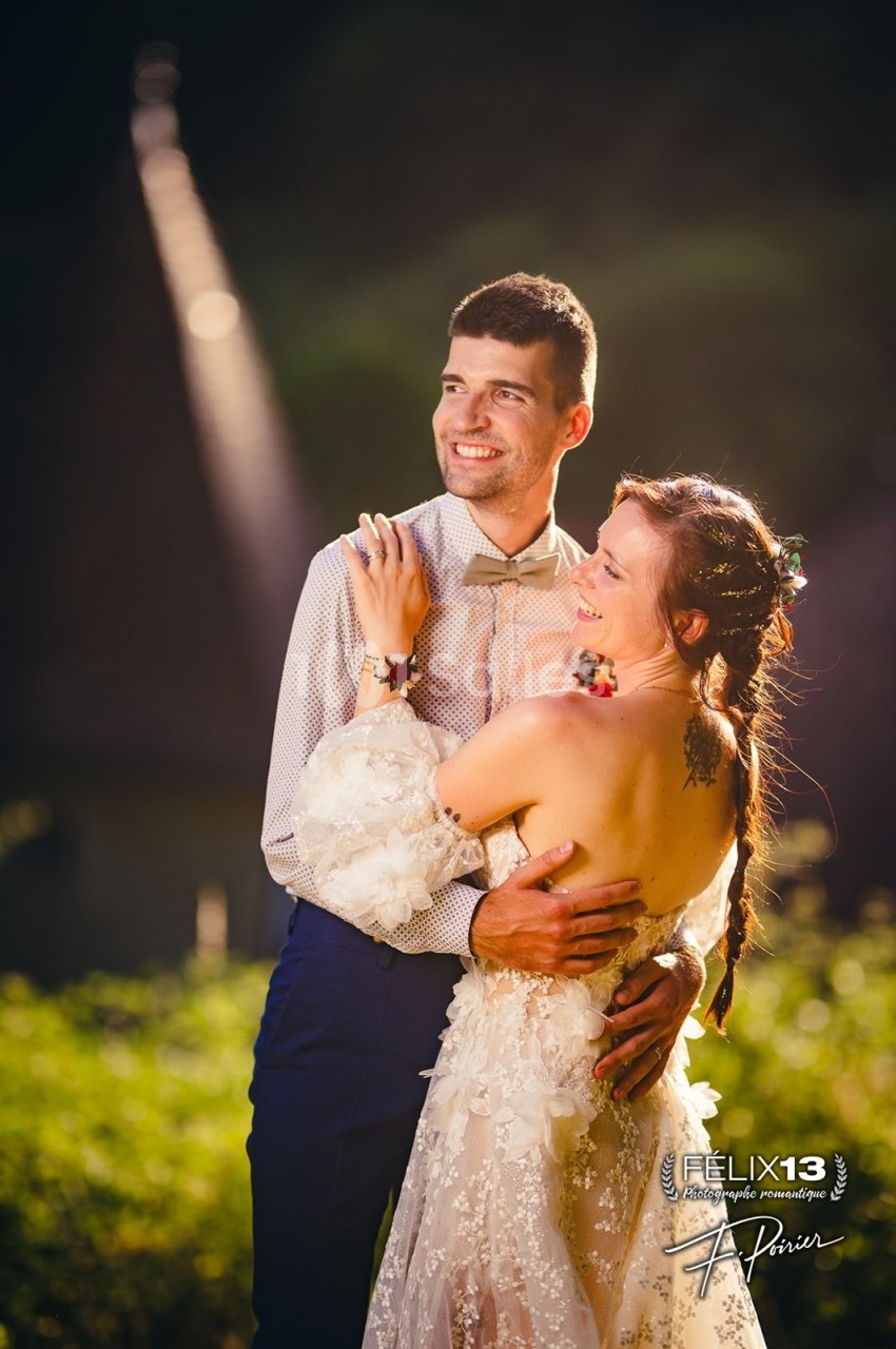 Un couple souriant en tenue de mariage, enlacé dans un cadre extérieur avec une lumière douce en arrière-plan.