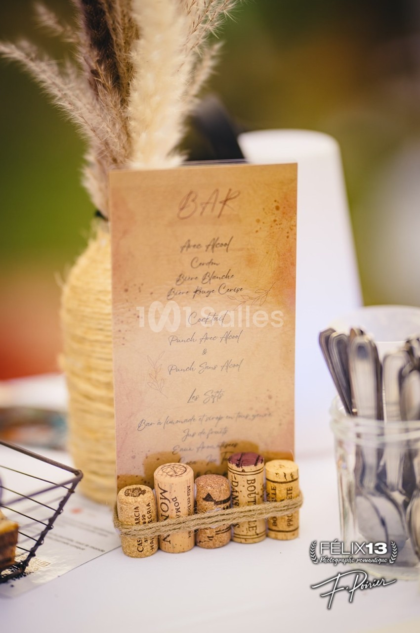 Carte de bar en papier beige avec une liste de boissons, décorée de bouchons de liège et d'herbes sèches.