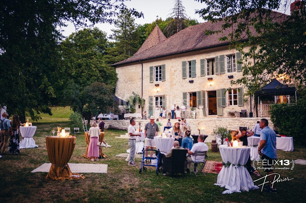 Personnes rassemblées dans un jardin devant une grande maison en pierre, lors d'une réception en plein air.