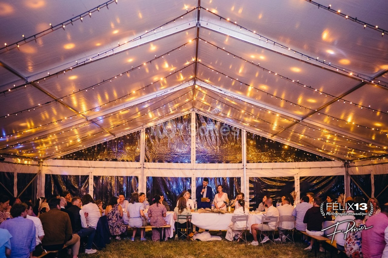Dîner festif sous une tente éclairée de guirlandes lumineuses, avec des invités assis autour de tables.