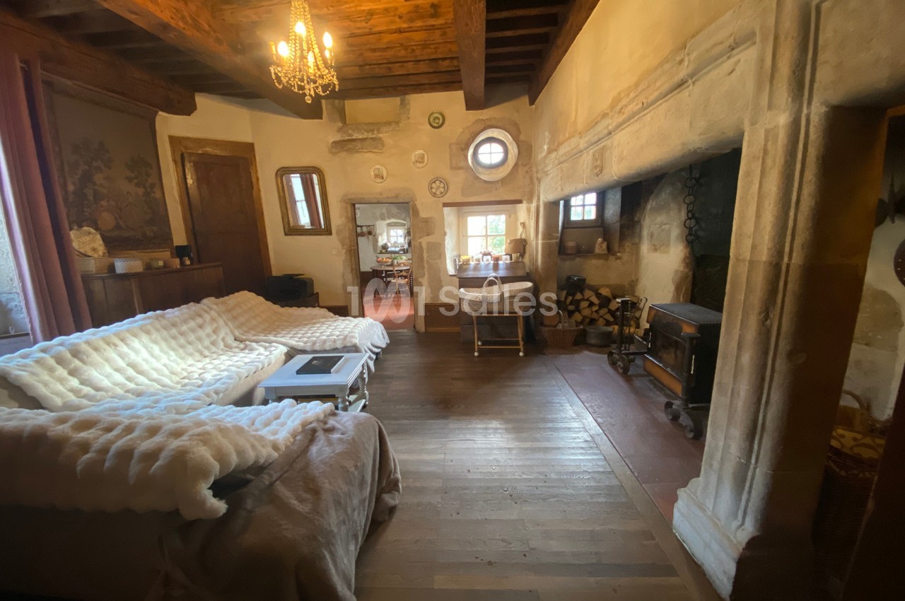 Salon rustique avec poutres apparentes, cheminée en pierre, canapé couvert d’un plaid et lumière naturelle.