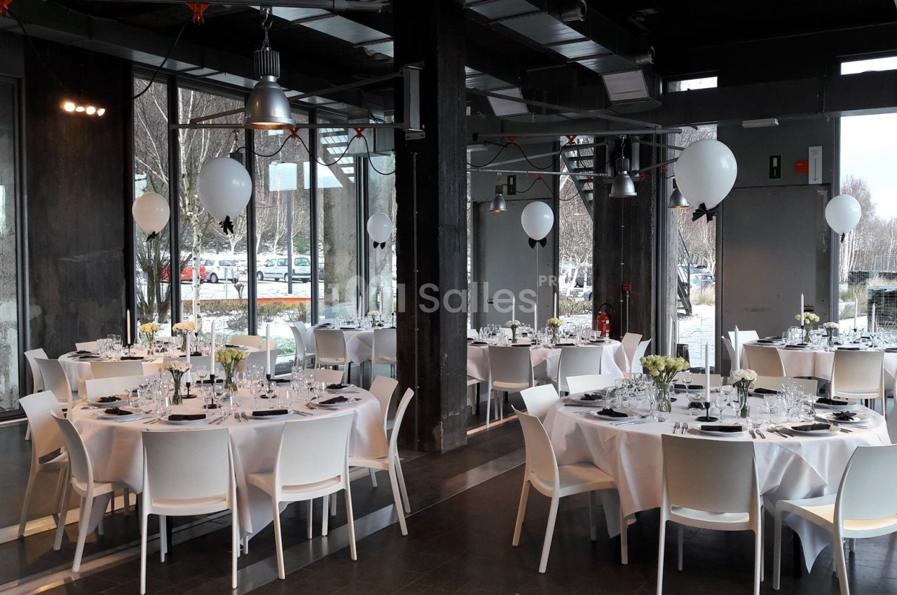 Salle de réception moderne avec tables rondes dressées, nappes blanches et décorations de ballons.