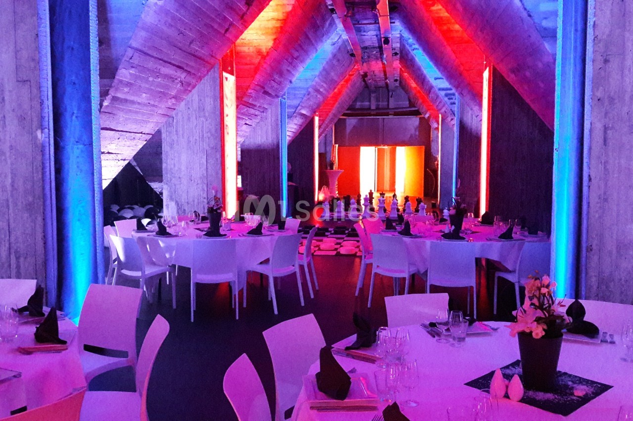 Salle de réception avec tables dressées, éclairage coloré rouge et bleu, et ambiance moderne.