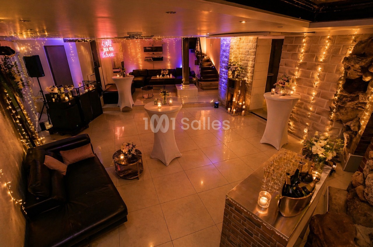 Salle décorée pour un événement, avec tables hautes, guirlandes lumineuses et ambiance chaleureuse.