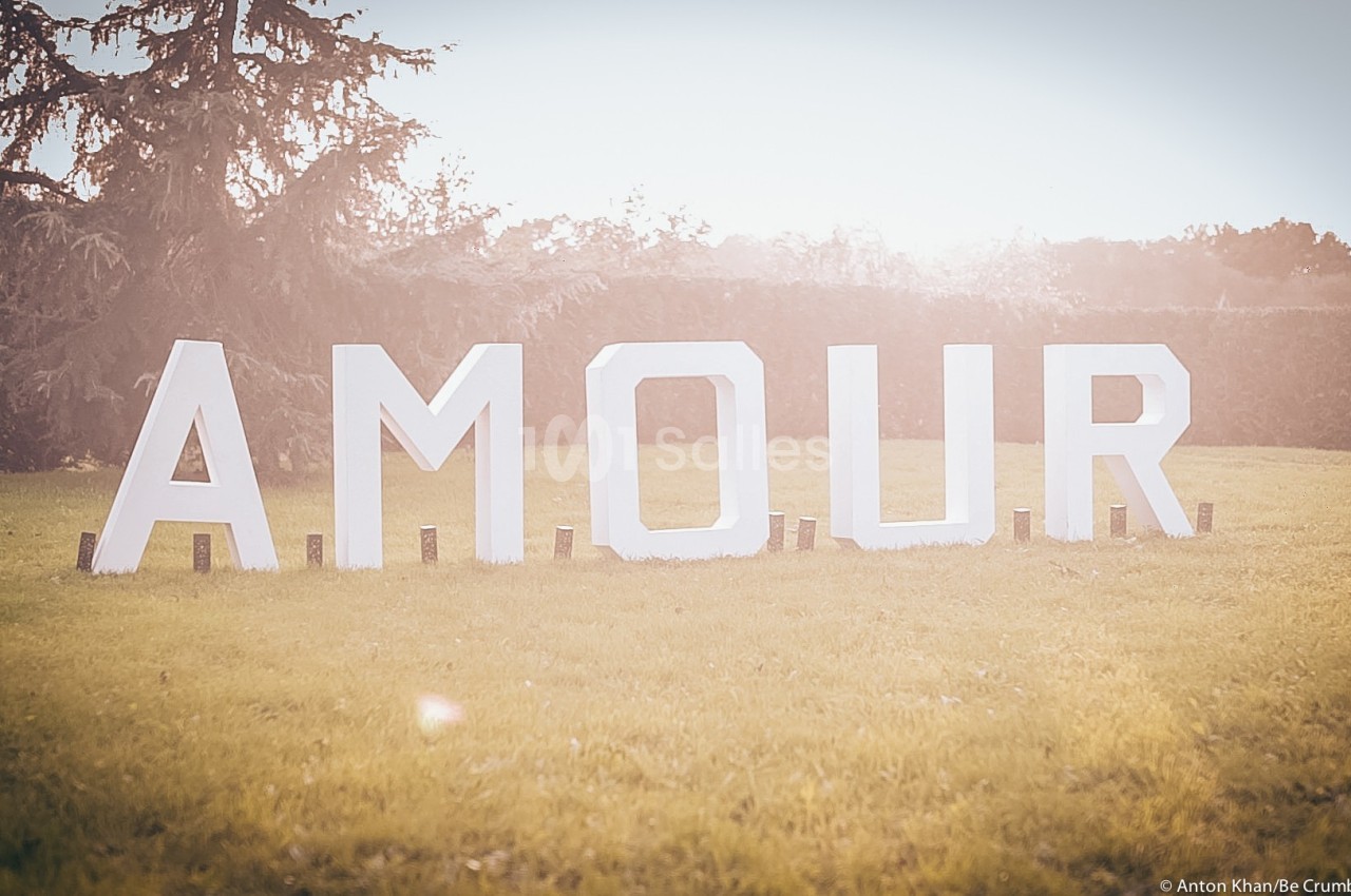 Lettres blanches formant le mot ’AMOUR’ disposées sur une pelouse, éclairées par une lumière douce au coucher du soleil.