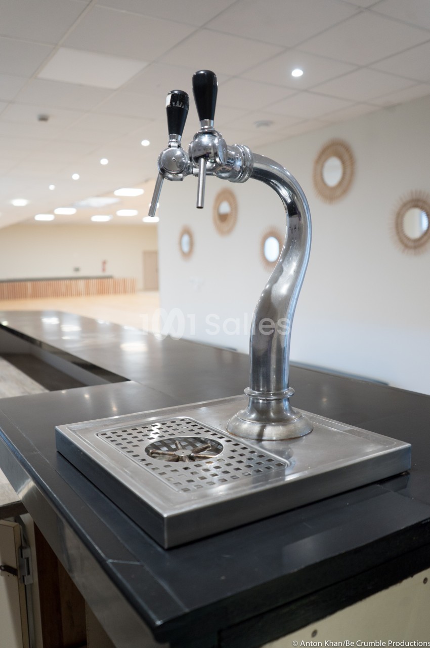 Robinet de distribution de boissons avec deux poignées noires, installé sur un comptoir en métal dans une salle lumineuse.