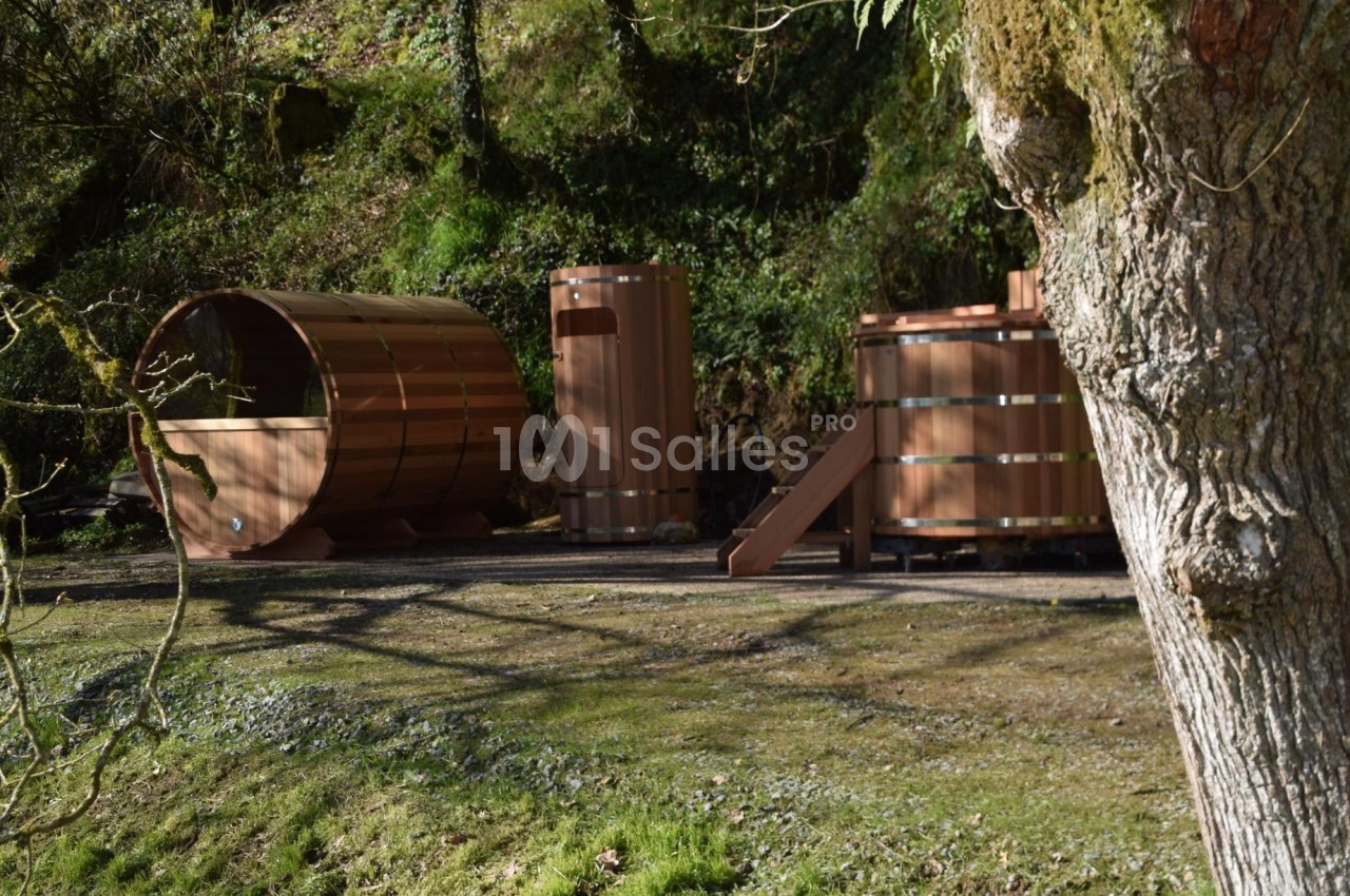 Installations en bois comprenant un sauna, une douche extérieure et un bain nordique dans un cadre naturel boisé.