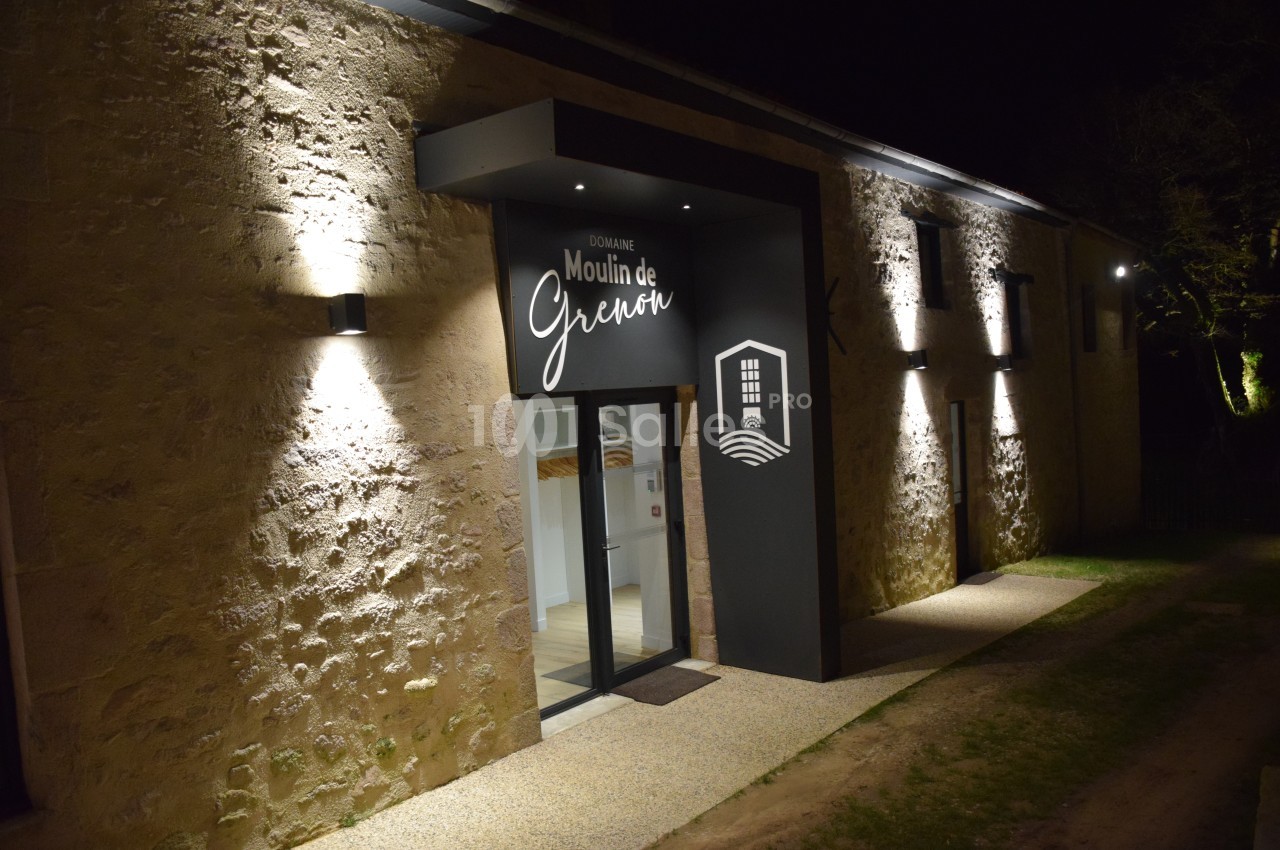 Entrée éclairée d'un bâtiment en pierre avec une enseigne ’Domaine Moulin de Giverny’ visible de nuit.