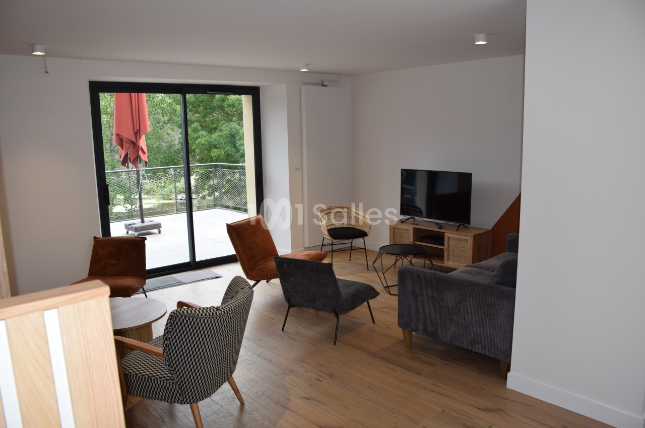 Salon moderne avec parquet, mobilier varié, télévision et grande baie vitrée donnant sur une terrasse arborée.