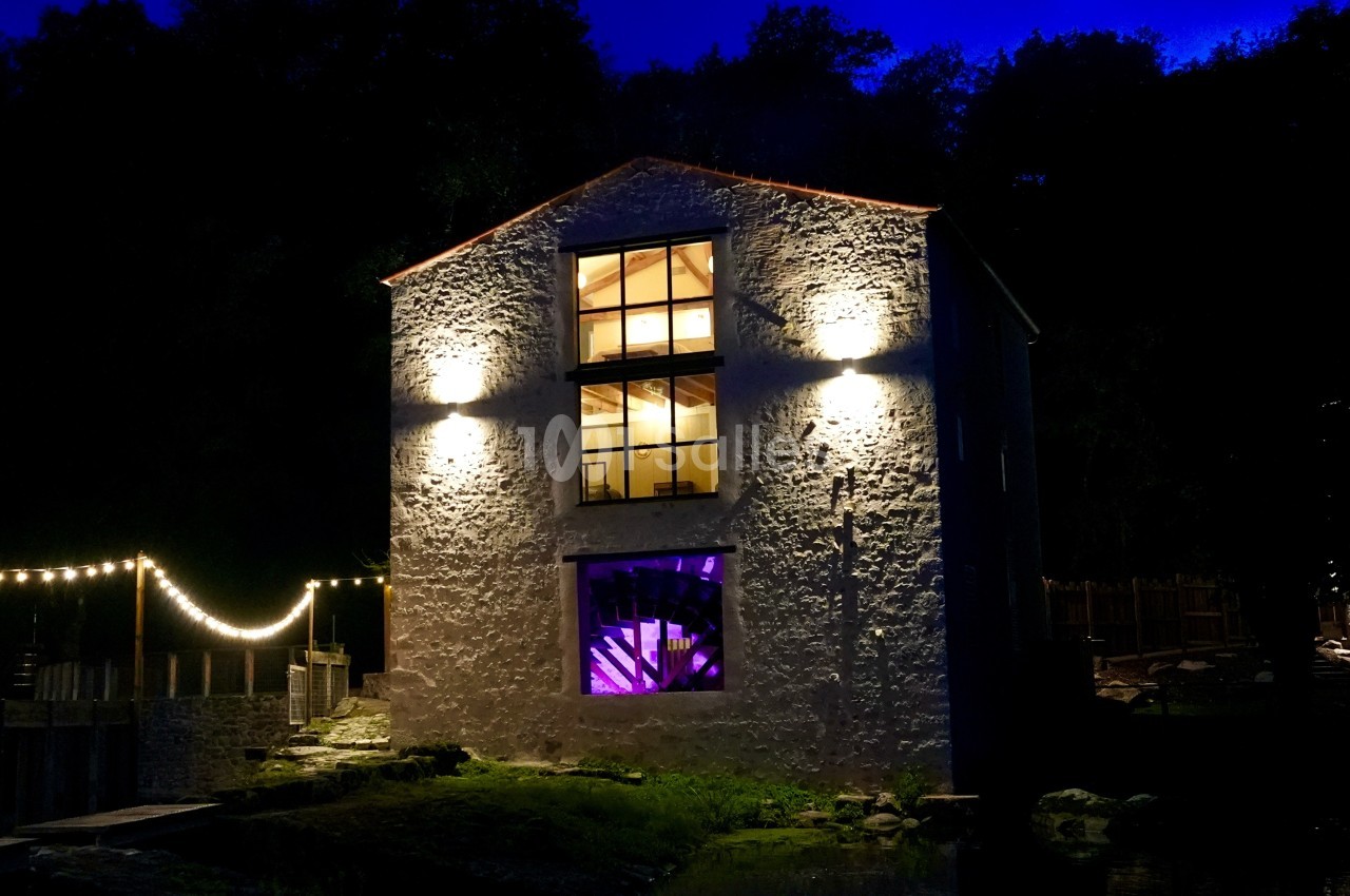 Façade d'un bâtiment en pierre éclairé la nuit, avec des lumières décoratives et une fenêtre illuminée en violet.
