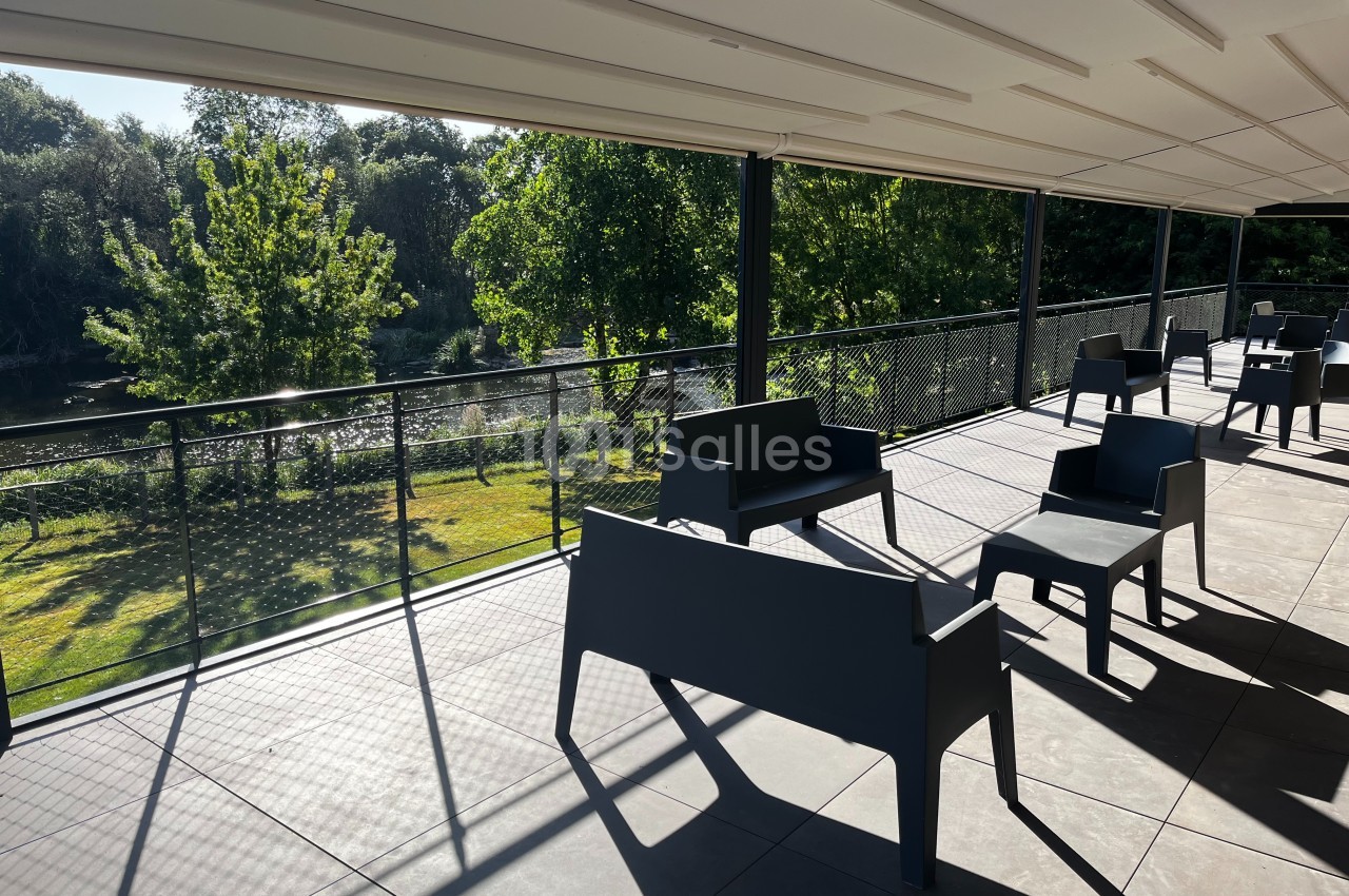 Terrasse ombragée avec des bancs noirs, vue sur un jardin verdoyant et une rivière en arrière-plan.