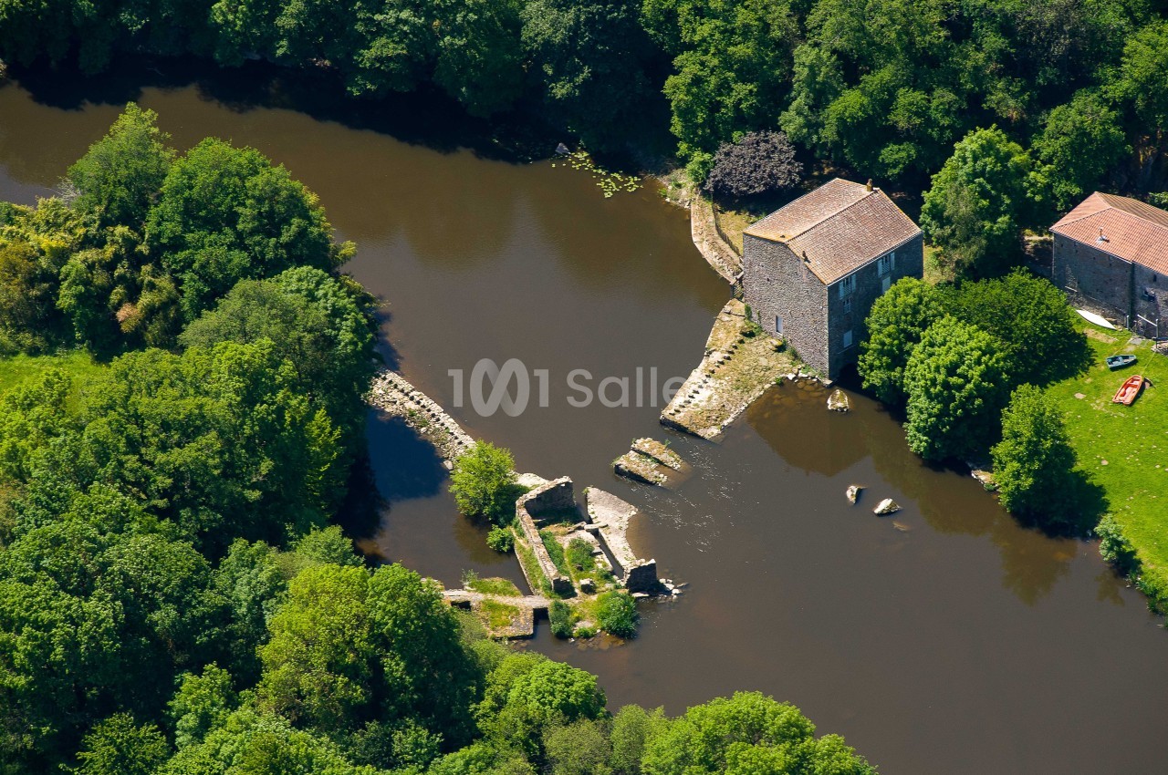 Vue aérienne d'un ancien moulin en pierre bordant une rivière entourée de végétation dense.