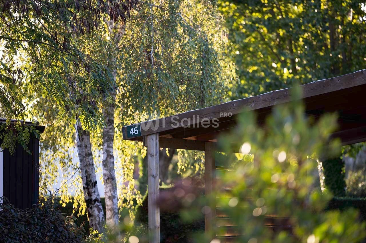 Abri en bois avec le numéro 46, entouré d'arbres et de feuillage sous une lumière naturelle.