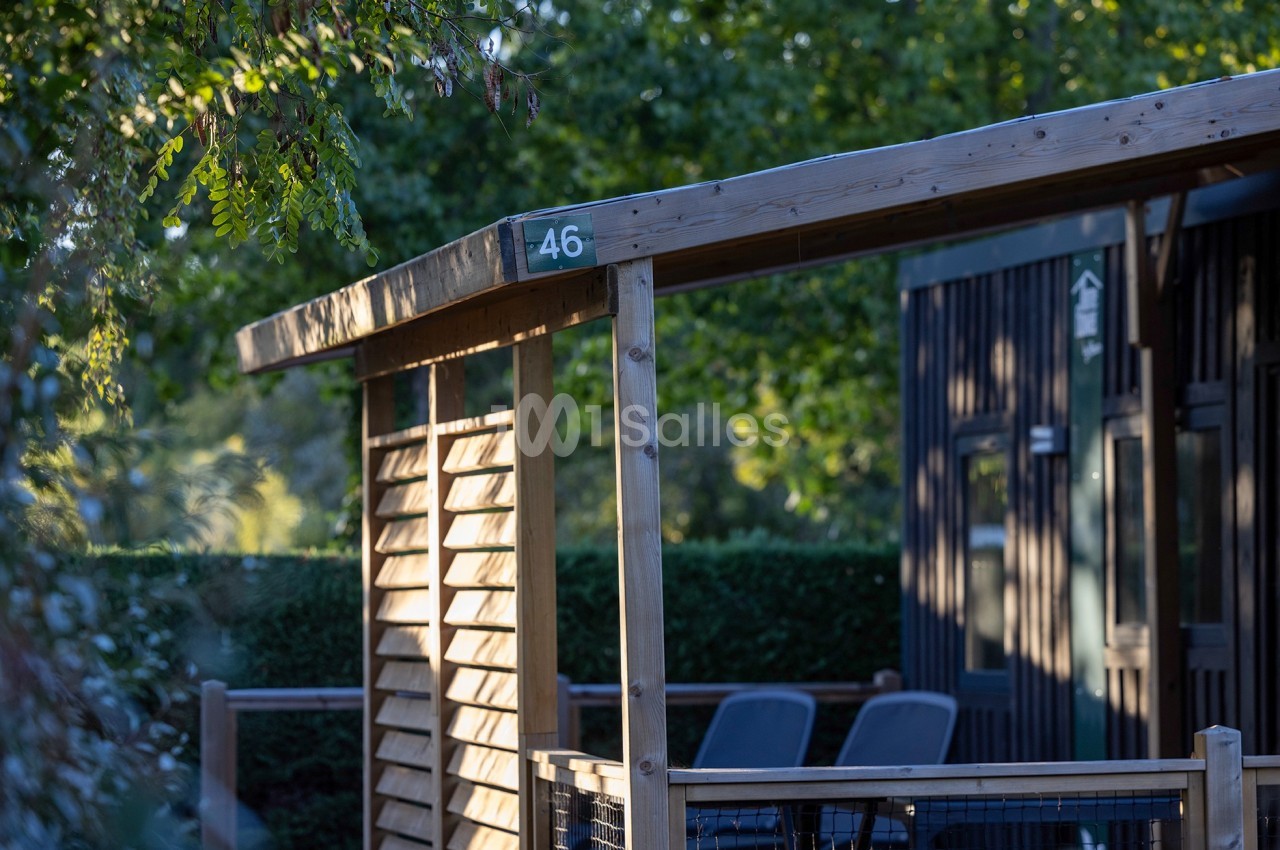 Terrasse en bois avec un numéro 46, entourée de verdure et partiellement ombragée par des arbres.