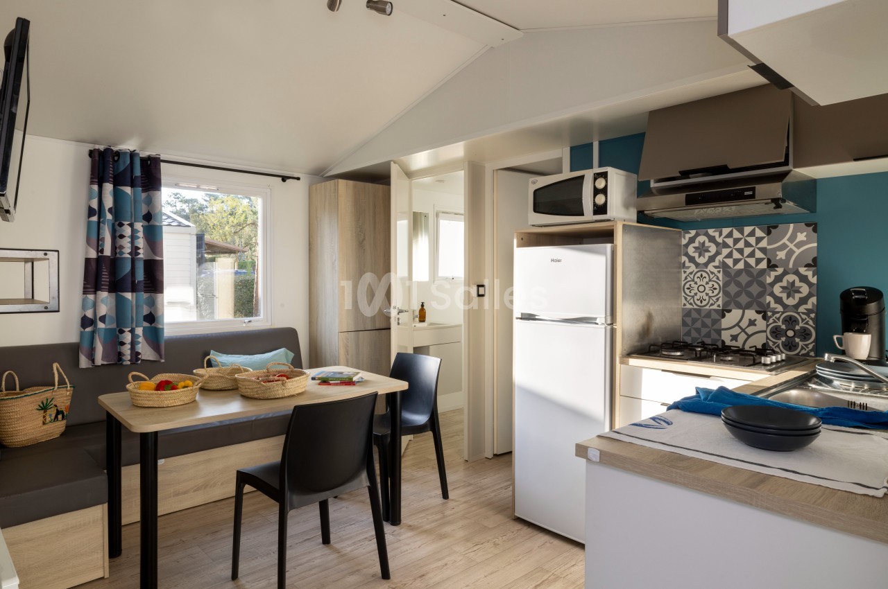 Intérieur d'une cuisine ouverte avec coin repas, réfrigérateur, micro-ondes, plaques de cuisson et décoration moderne.