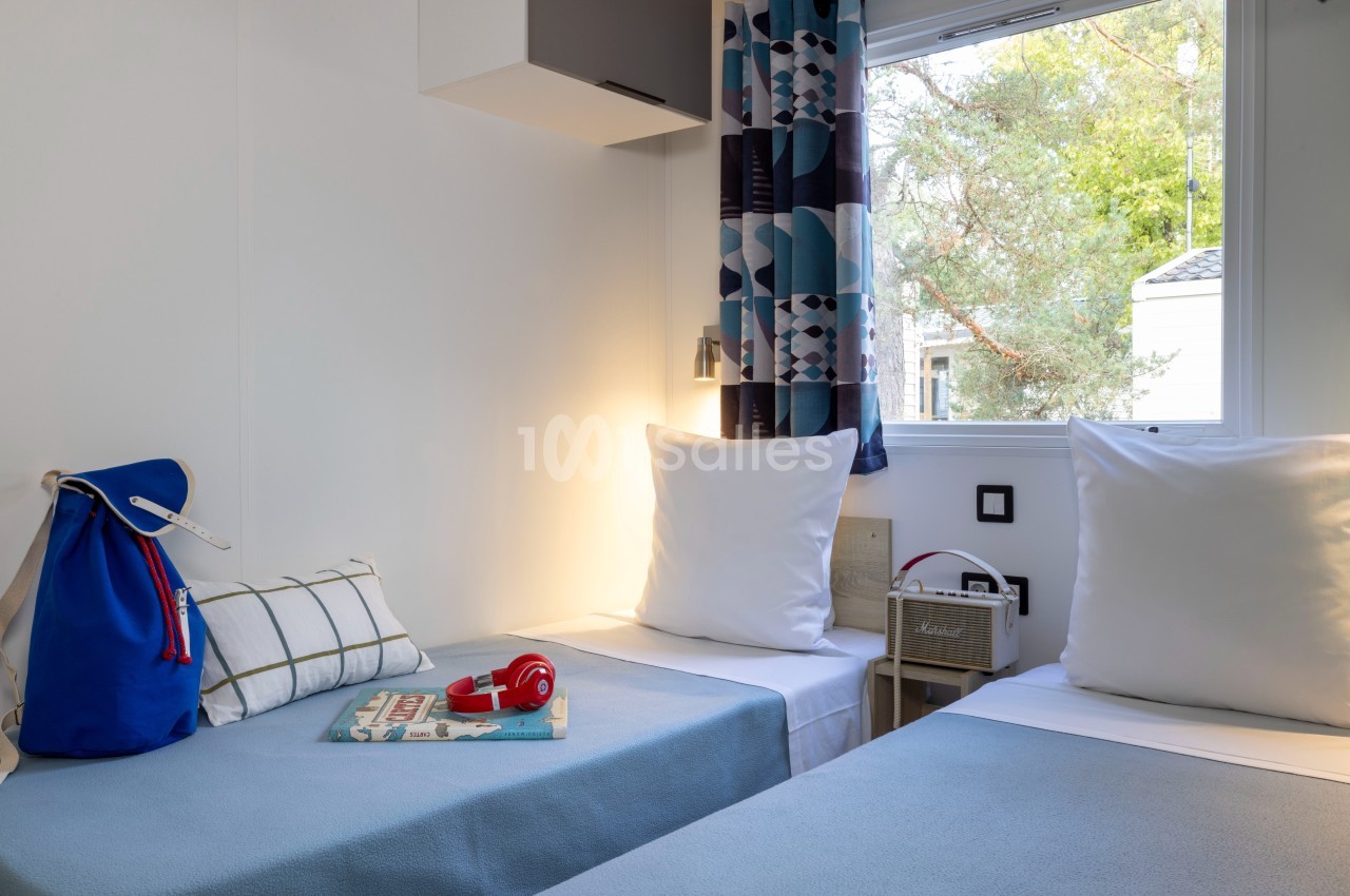 Chambre lumineuse avec deux lits simples, une fenêtre donnant sur l'extérieur et des objets de décoration simples.