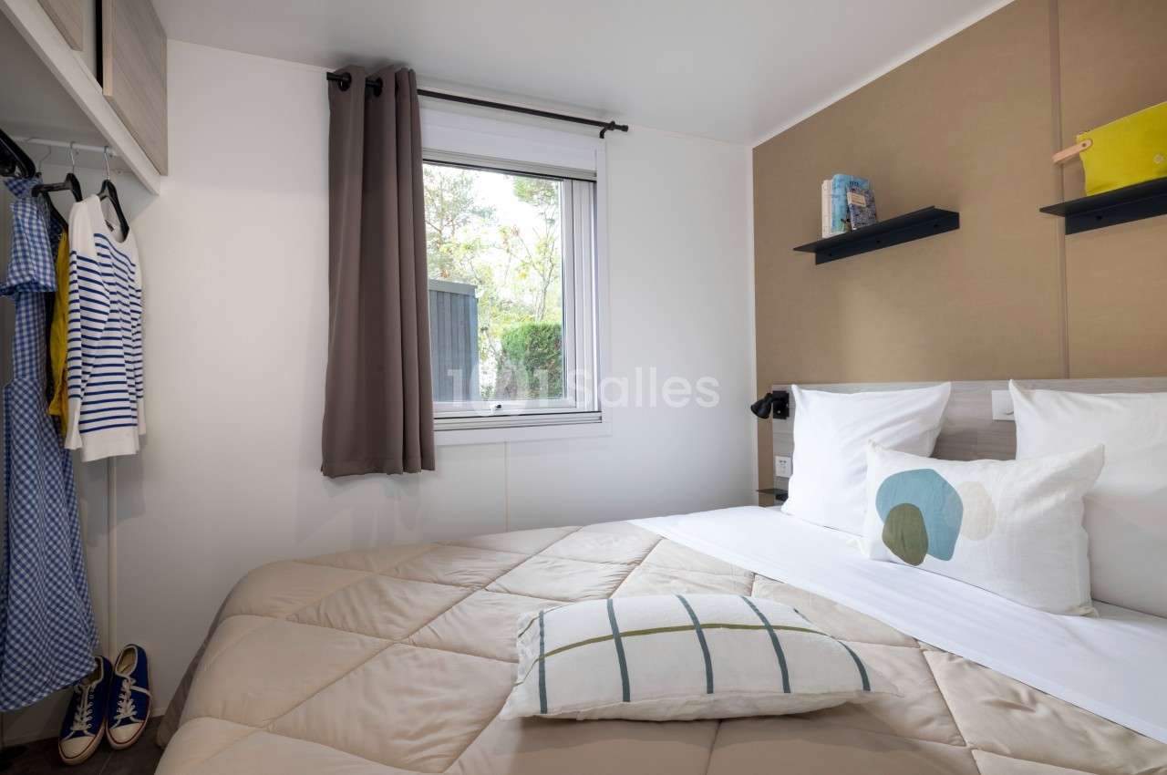 Chambre lumineuse avec lit double, étagères murales, fenêtre donnant sur l'extérieur et vêtements suspendus.