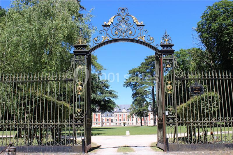 Grille en fer forgé ornée ouvrant sur un parc avec un bâtiment historique en arrière-plan.