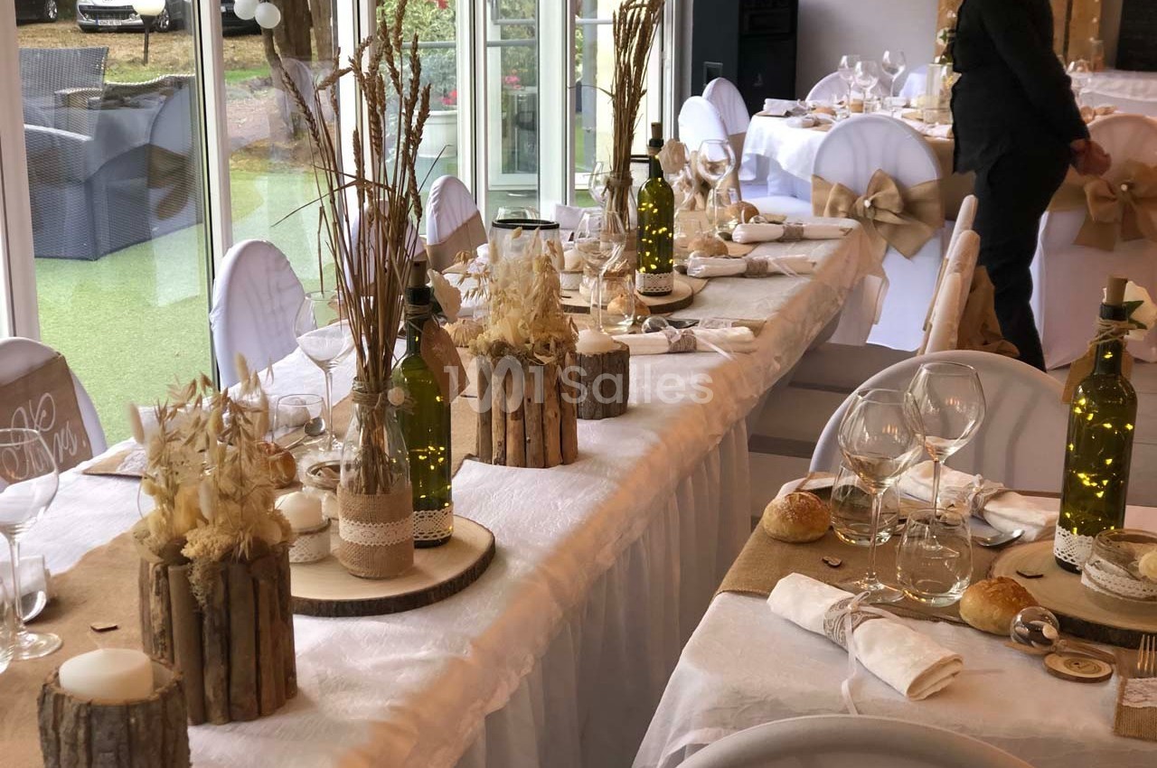 Salle de réception décorée avec des tables dressées, ornées de centres de table rustiques et d'éléments naturels.