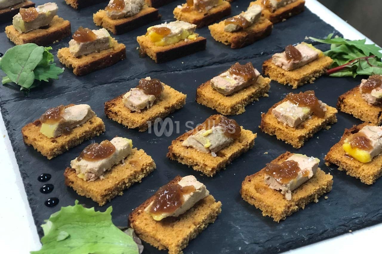 Toasts de pain d'épices garnis de foie gras et chutney, disposés sur une ardoise avec quelques feuilles de salade.