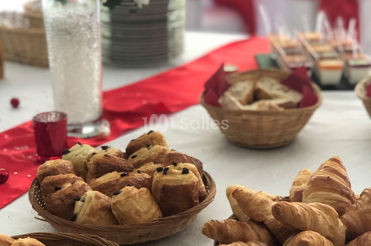 Assortiment de viennoiseries dans des paniers en osier sur une table décorée avec une nappe blanche et un chemin de table…