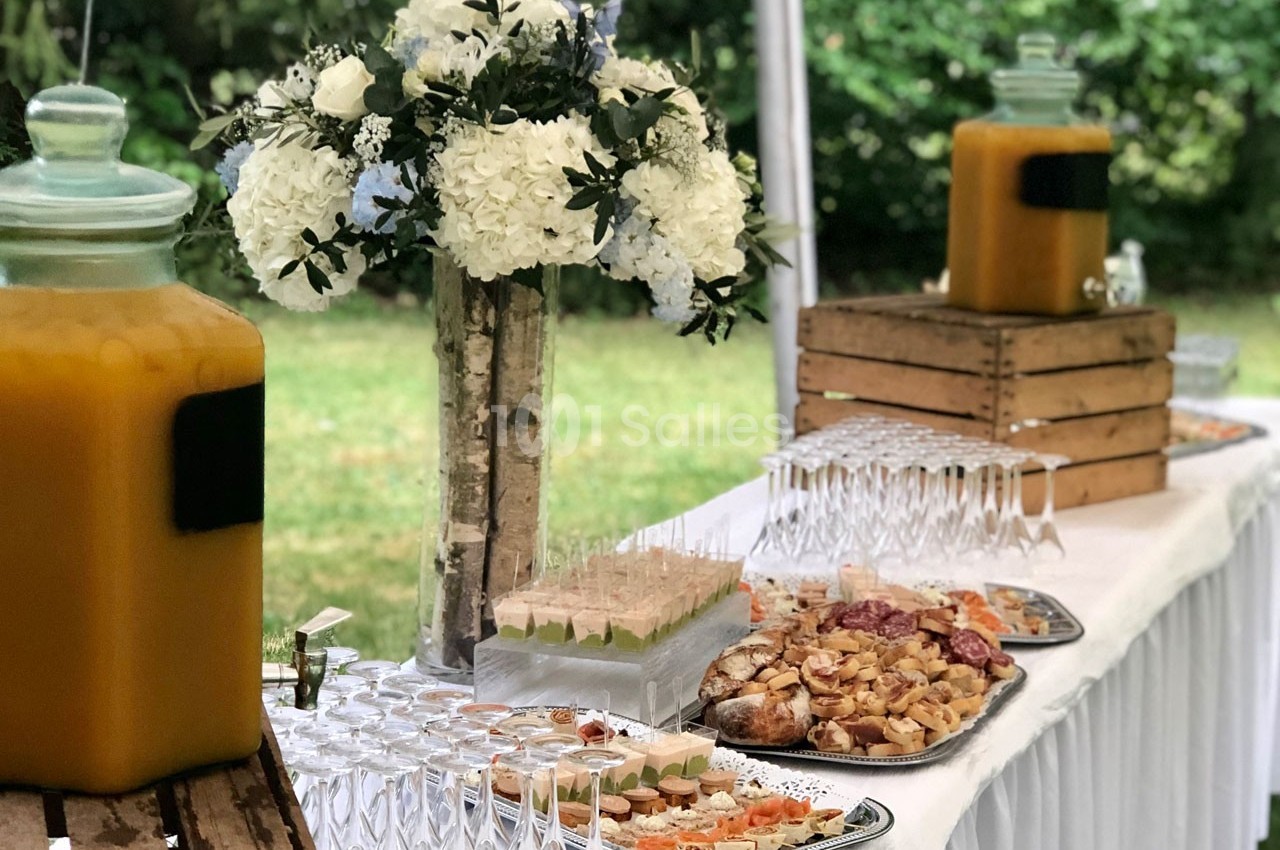 Buffet en extérieur avec boissons, fleurs blanches en décoration et plats variés disposés sur une table blanche.