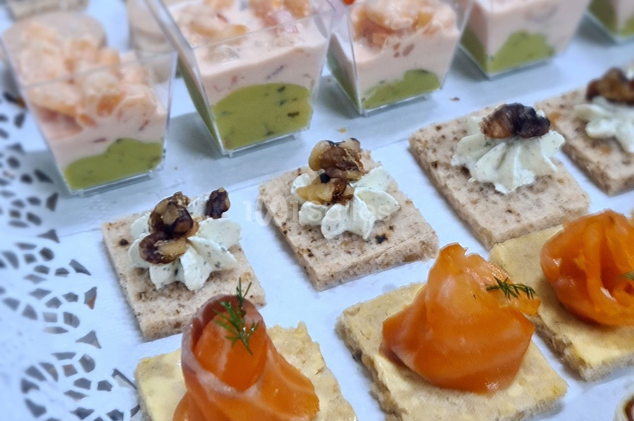 Assortiment de canapés avec saumon fumé, crème aux noix et verrines de crevettes sur une nappe blanche.
