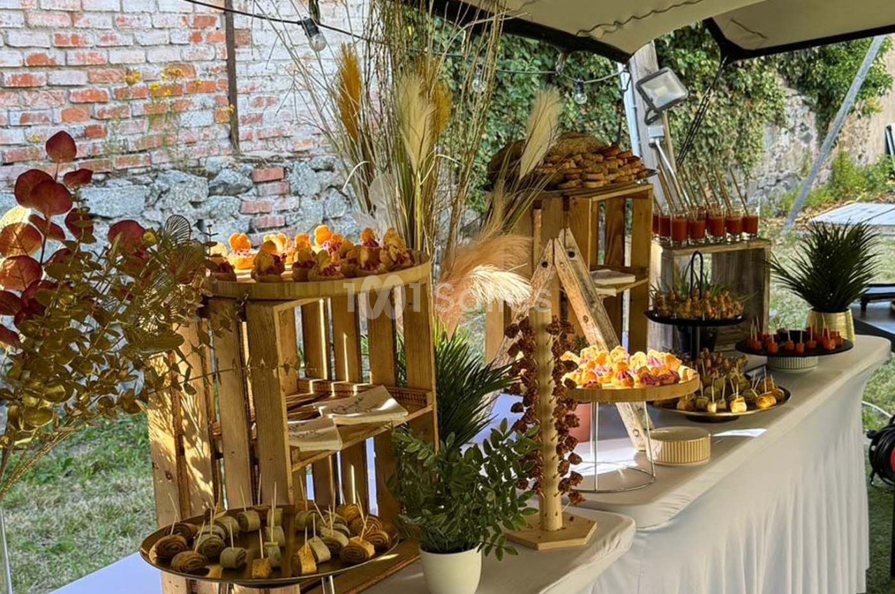 Buffet en plein air avec présentation soignée de mets variés sur des supports en bois et décorations végétales.