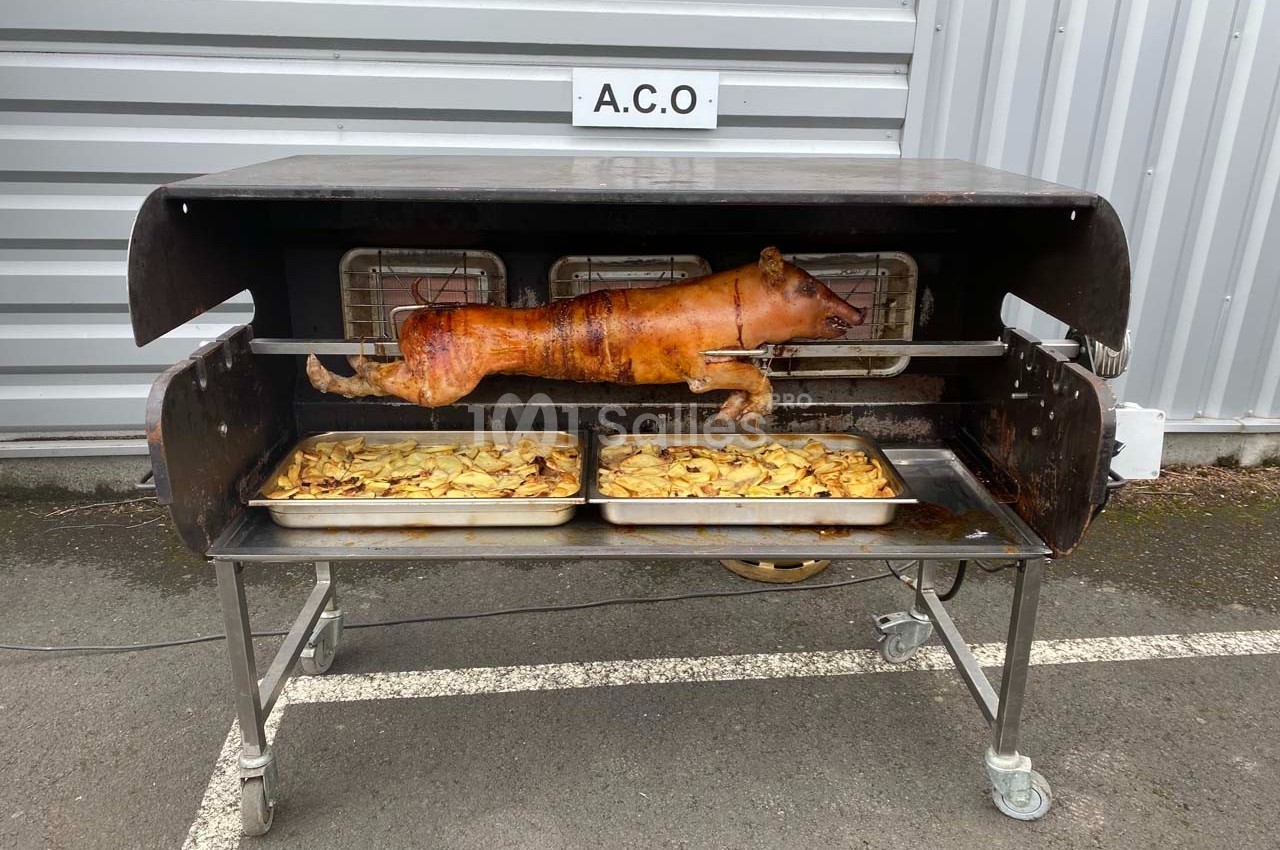 Porcelet entier rôti à la broche au-dessus de plateaux de pommes de terre, dans un four en extérieur.