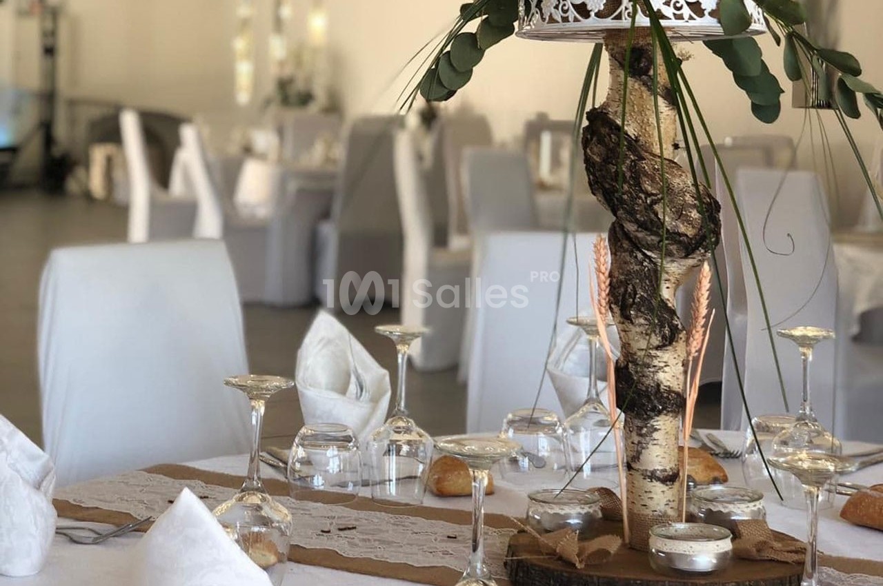 Table décorée pour un événement avec centre de table en bois et feuillage, nappes blanches et verres disposés.