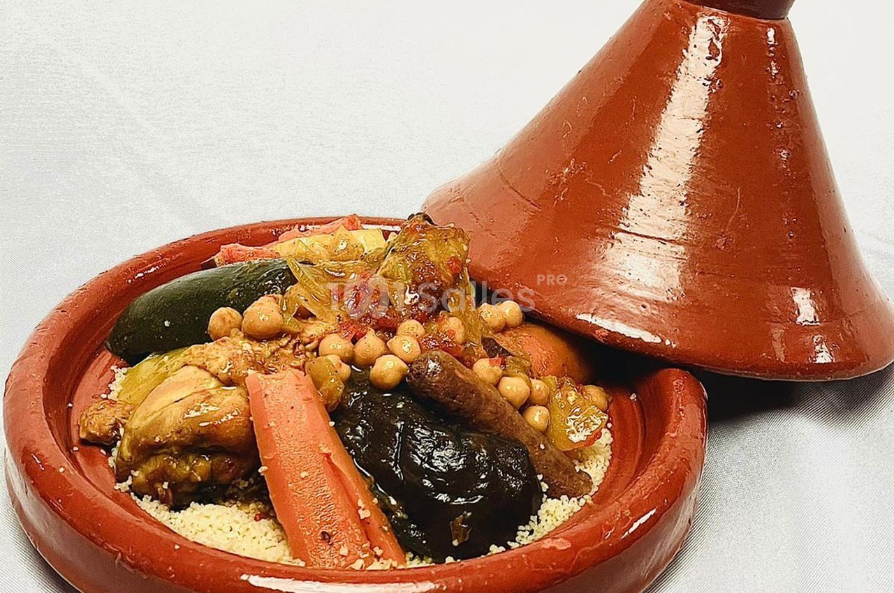 Plat de tajine en terre cuite contenant légumes, pois chiches, pruneaux et viande, accompagné de semoule.