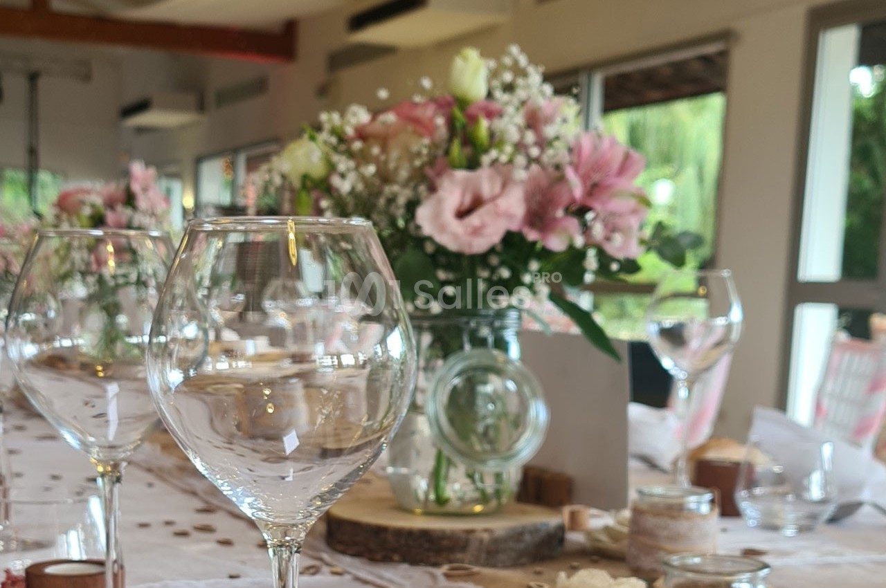 Table décorée avec des verres à vin, des bougies et un bouquet de fleurs roses et blanches dans une salle lumineuse.