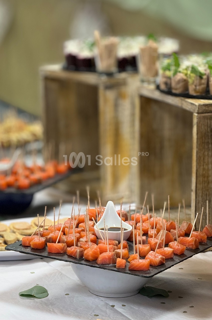 Plateau de bouchées de saumon sur des pics en bois, entouré d'autres amuse-bouches sur une table de réception.