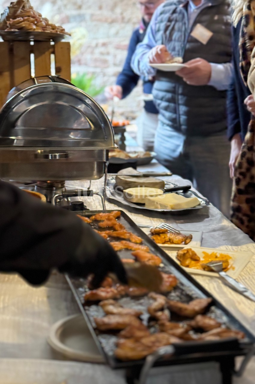 Buffet avec des plats chauds, des grillades et des convives se servant dans une ambiance conviviale.
