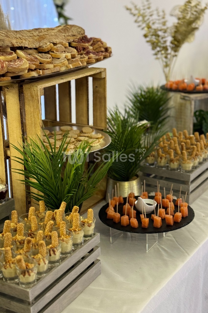 Buffet avec verrines, brochettes apéritives, pains garnis et décorations végétales sur une table blanche.