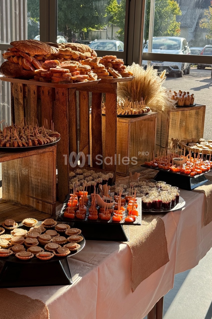 Buffet de réception avec assortiments de bouchées salées et sucrées présentés sur des plateaux et des caisses en bois.