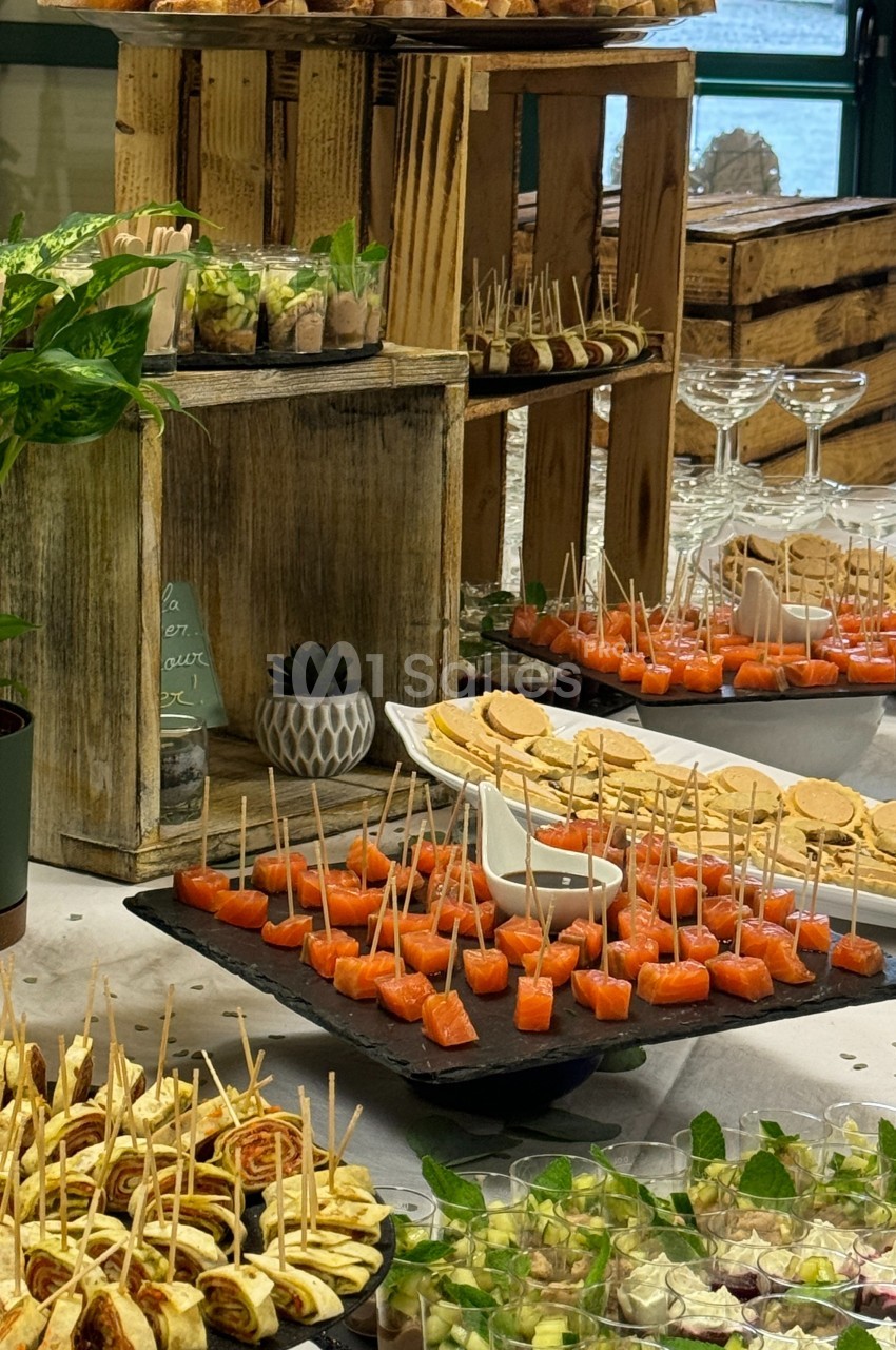 Buffet avec divers amuse-bouches, incluant brochettes de saumon, verrines, toasts et présentoirs en bois rustique.