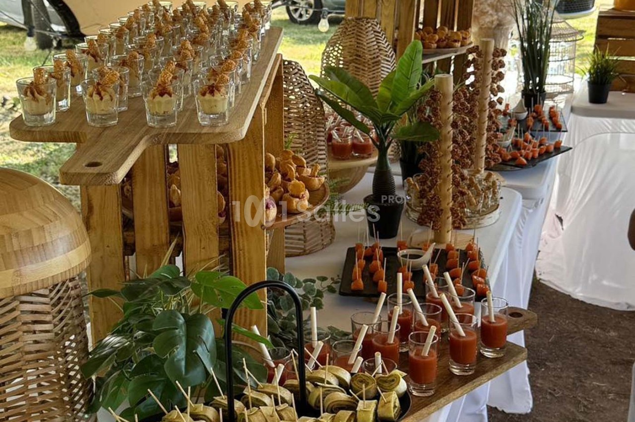 Buffet en plein air avec verrines, brochettes et assortiments de bouchées disposés sur des présentoirs en bois.