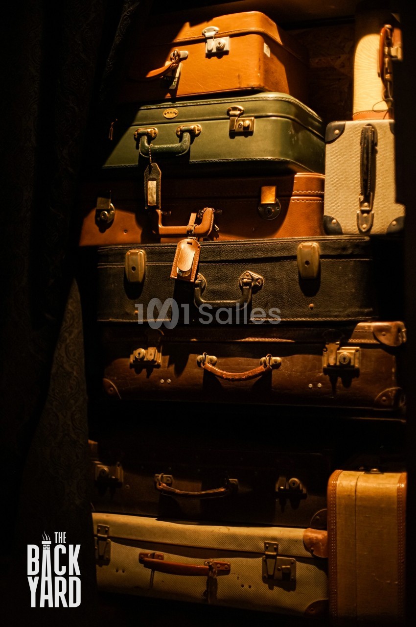 Pile de valises vintage en cuir et en tissu, de différentes tailles et couleurs, empilées dans un espace sombre.