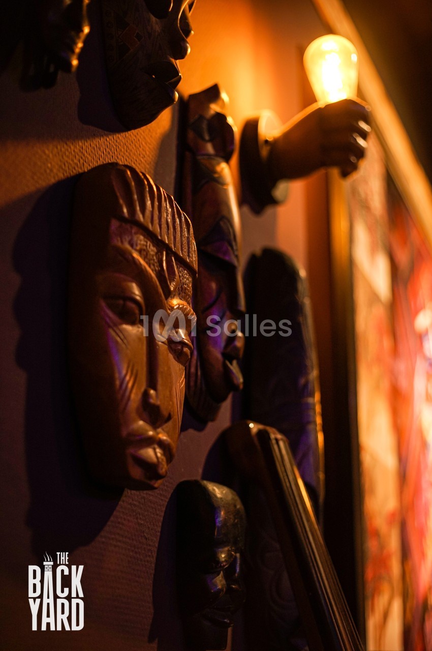 Masques en bois sculpté accrochés à un mur faiblement éclairé, avec une lumière chaude en arrière-plan.
