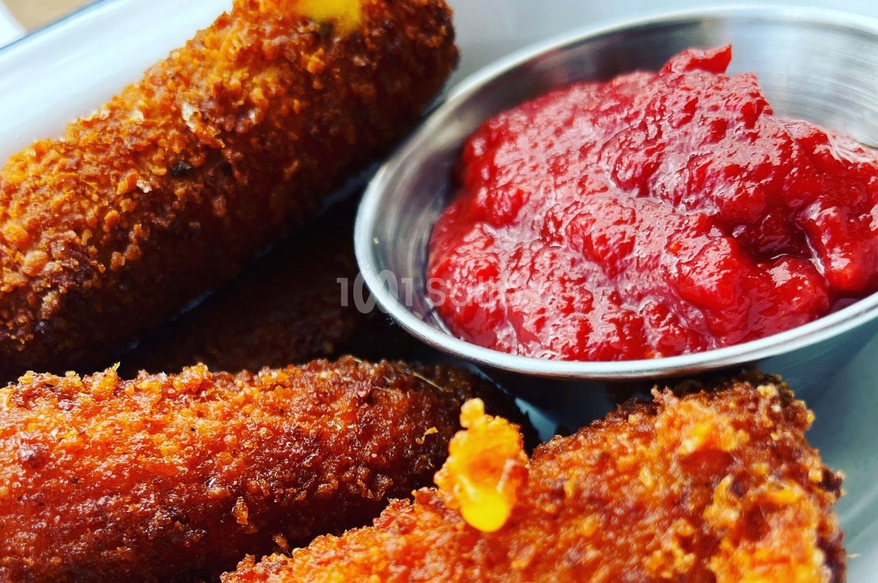 Bâtonnets de fromage panés dorés accompagnés d'une coupelle de sauce rouge.