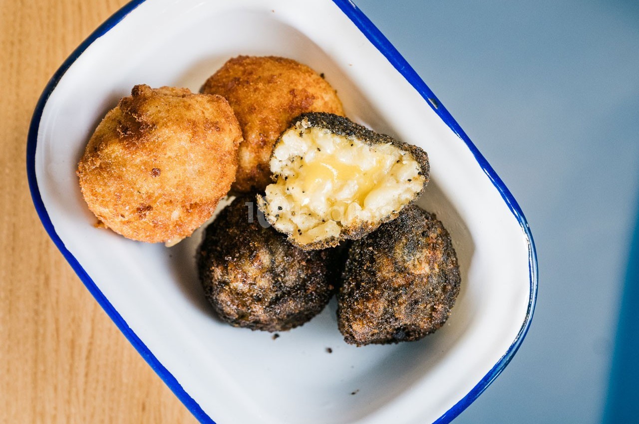 Quatre boulettes panées, dont une coupée révélant un cœur fondant, servies dans un plat émaillé blanc.