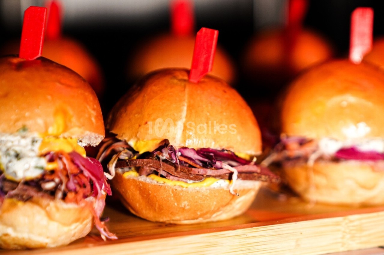 Petits burgers garnis de viande effilochée, coleslaw coloré et sauce, présentés sur une planche en bois.